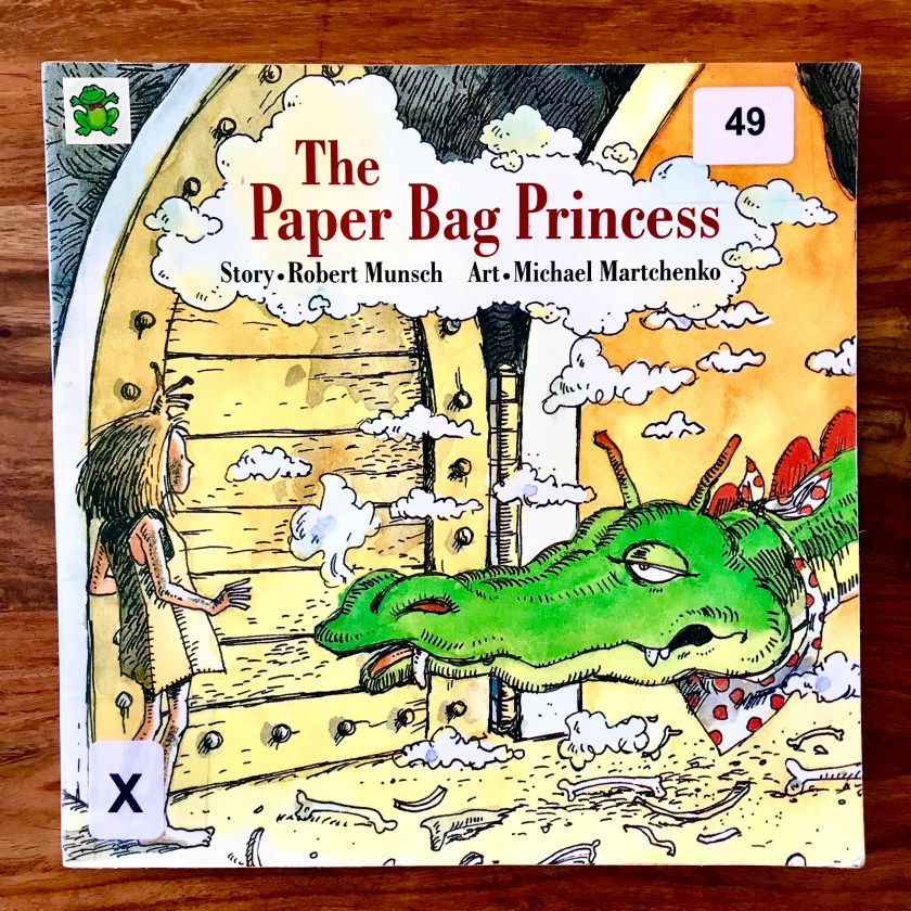 The image is a photograph of the cover of the book The Paper Bag Princess by Robert Munsch. The cover features an illustration of the paper bag princess facing a dragon.
