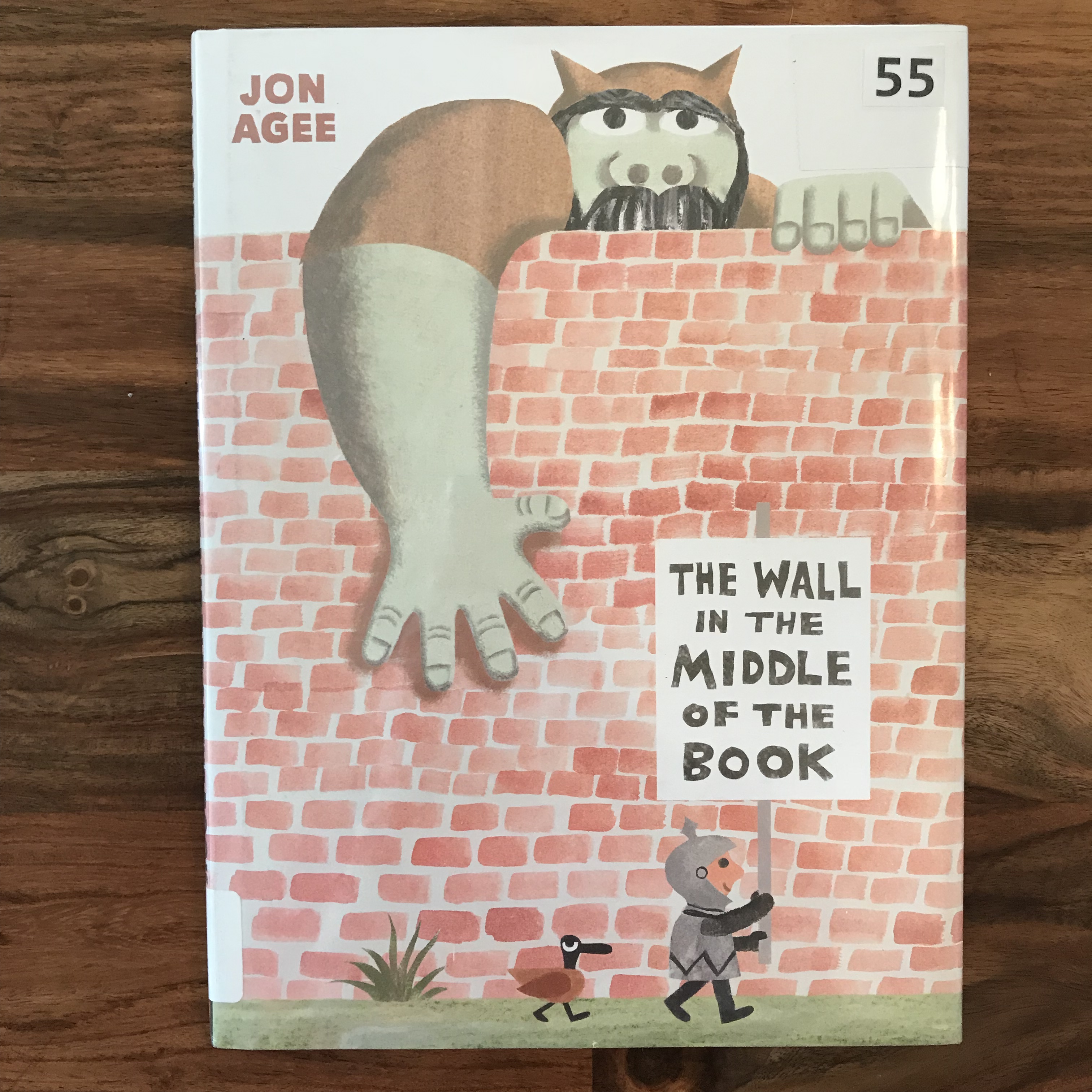 The cover of "The Wall in the Middle of the Book" shows a knight standing on one side of a brick wall holding a sign with the title of the book. Behind the wall is an ogre who is reaching a large hand over the top of the wall.